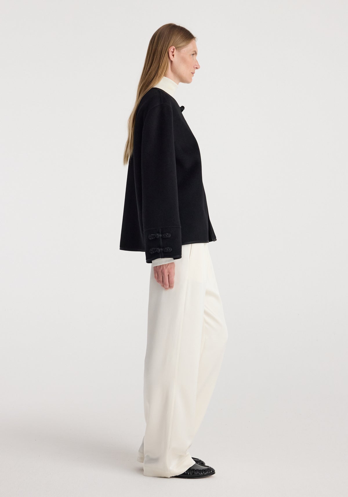 Profile view of a woman wearing a black Double-faced pankou jacket | black paired with white wide-leg pants and black shoes against a plain background.