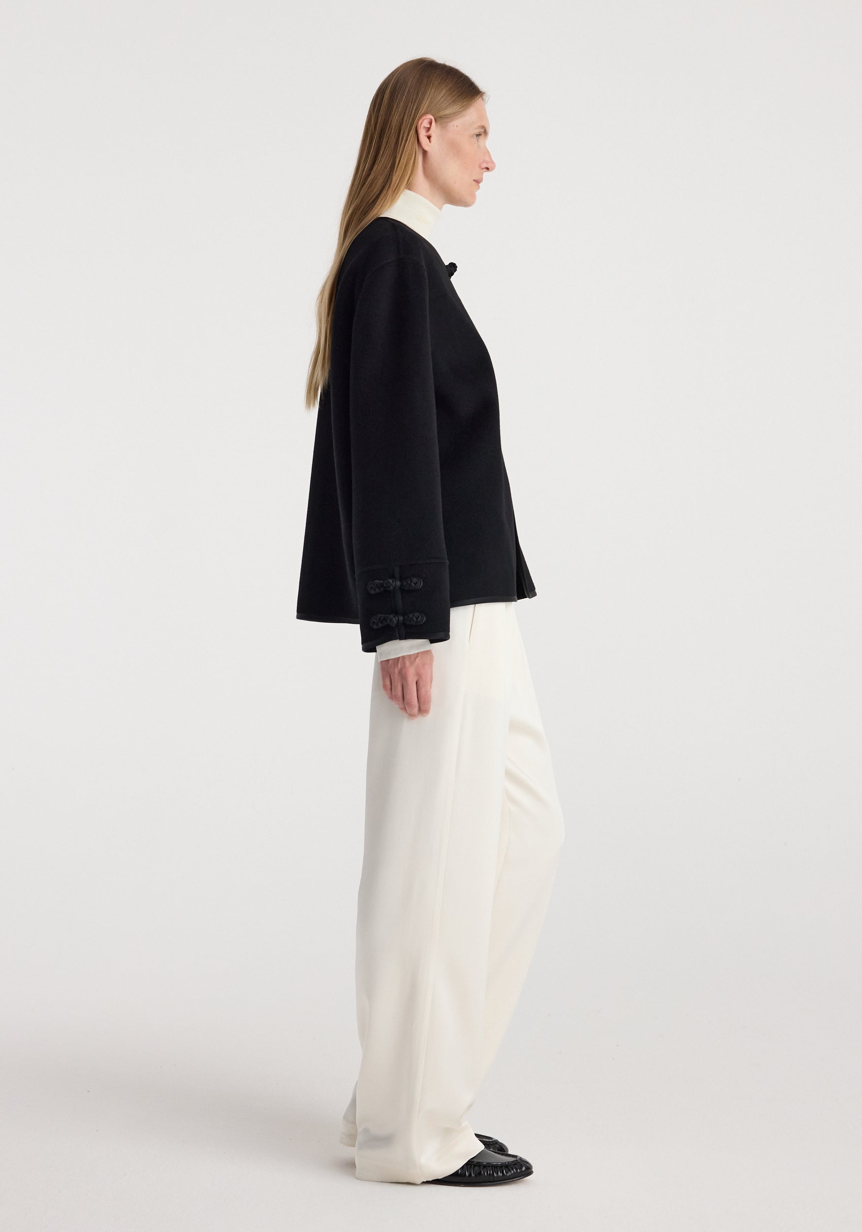 Profile view of a woman wearing a black Double-faced pankou jacket | black paired with white wide-leg pants and black shoes against a plain background.