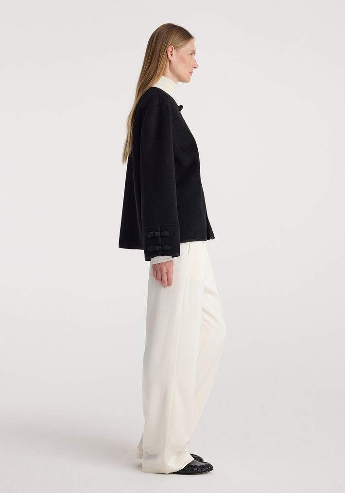 Profile view of a woman wearing a black Double-faced pankou jacket | black paired with white wide-leg pants and black shoes against a plain background.