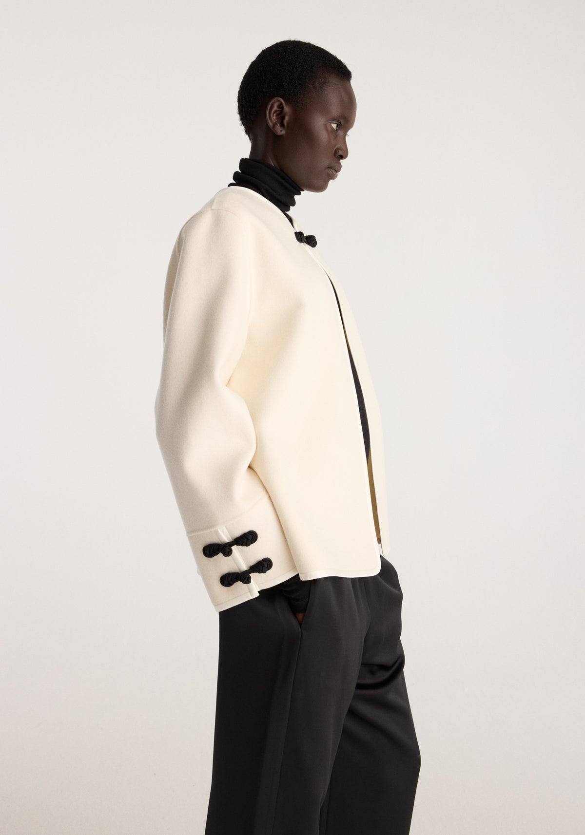 Double-faced pankou jacket | off white shown in side view on a model, featuring black toggle closures at the collar and sleeve cuffs with black trousers