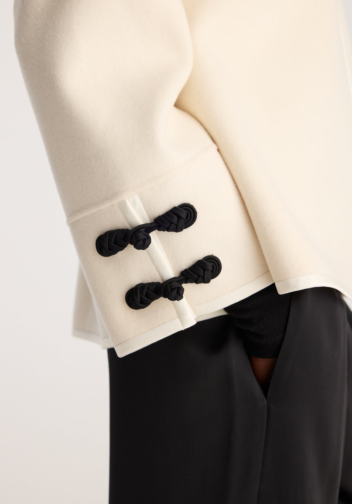Double-faced pankou jacket | off white showing black knotted fastenings at the side opening and sleeve over black trousers