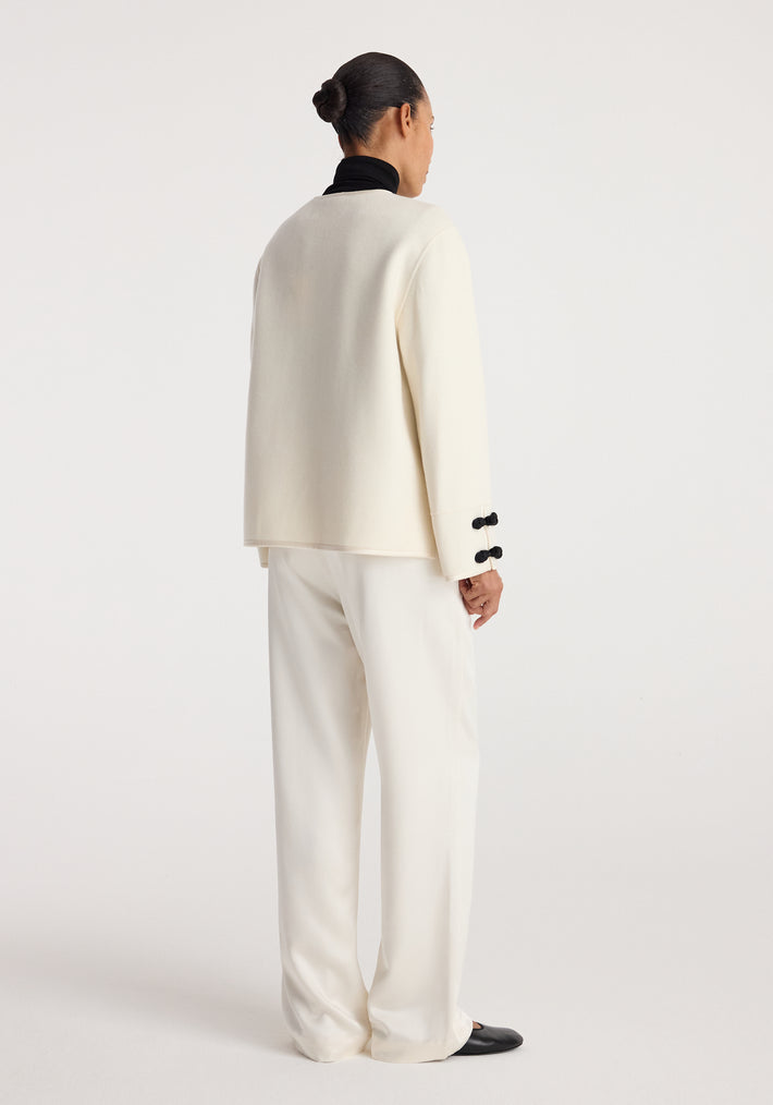 Back view of a person wearing a Double-faced pankou jacket | off white with black pankou button details on the cuffs, paired with loose off-white pants and black shoes.