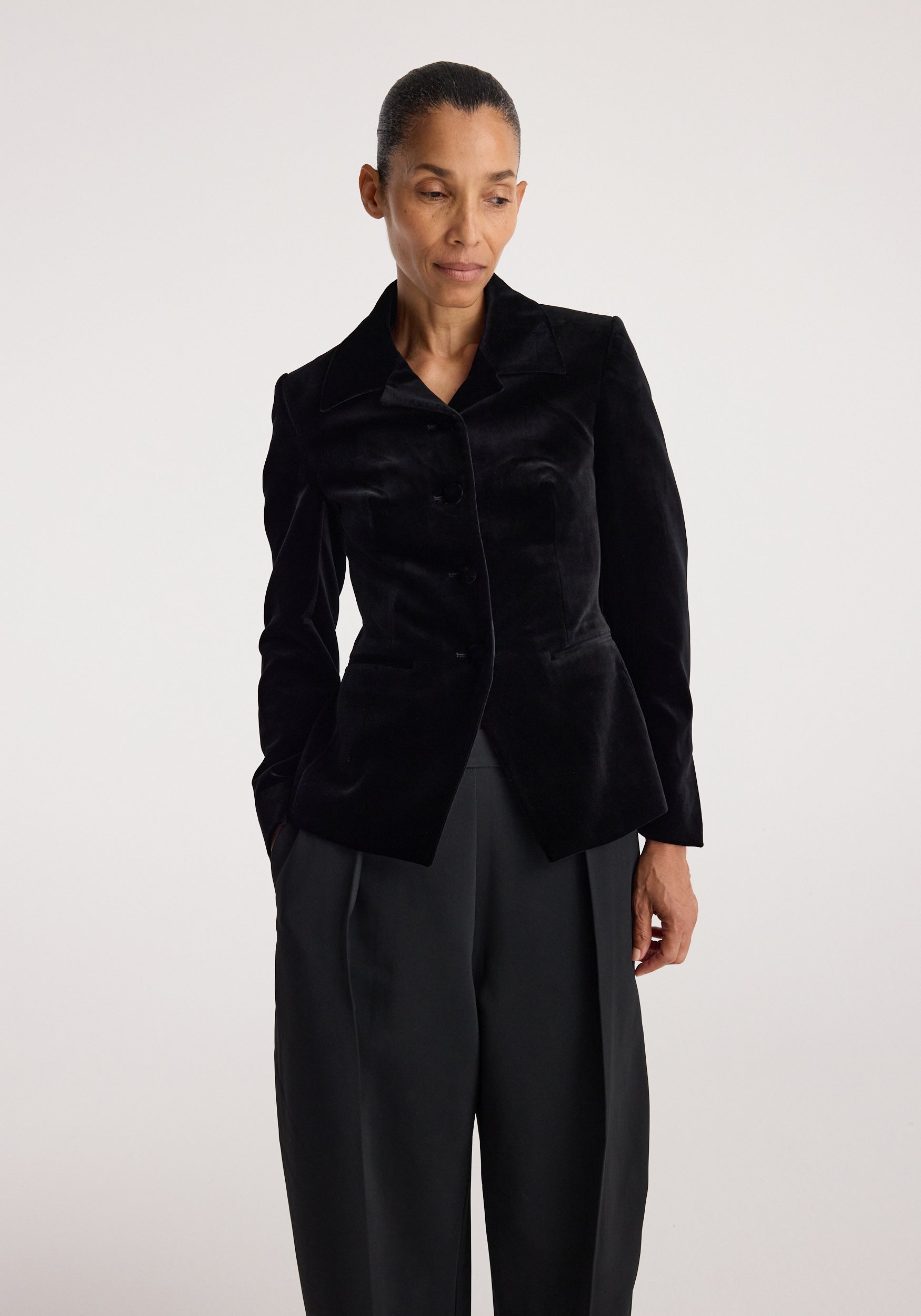 Woman wearing a Classic fitted velvet blazer | black with a tailored fit, buttoned front, and structured collar, paired with loose black trousers against a neutral background.