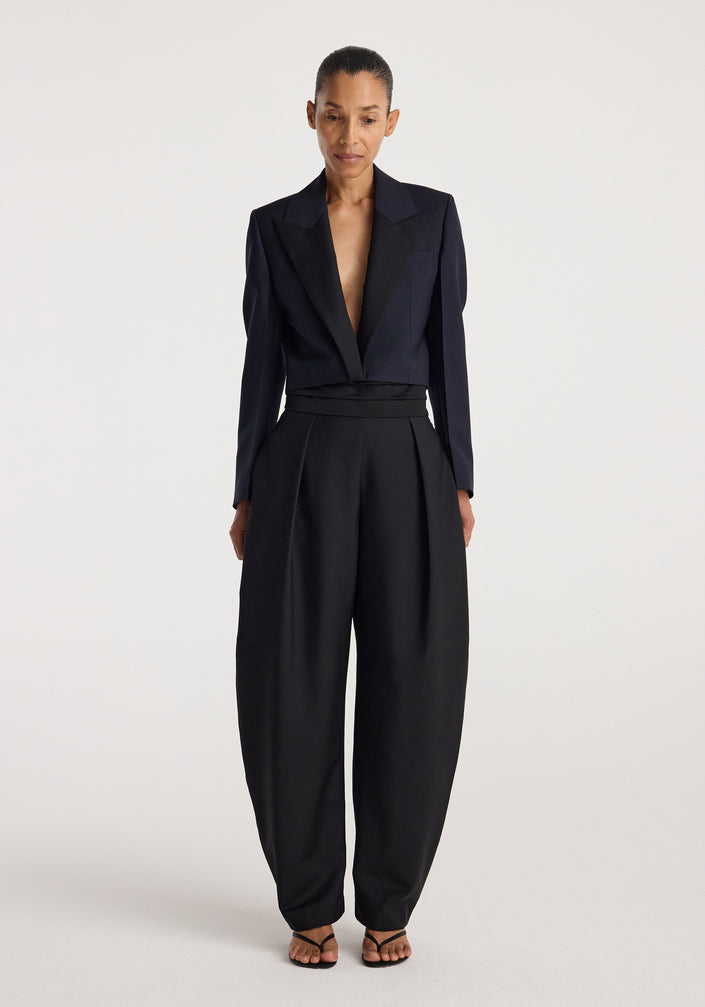 Woman wearing a tailored Cropped blazer | navy with a deep neckline paired with high-waisted wide-leg black trousers and strappy black sandals against a plain background