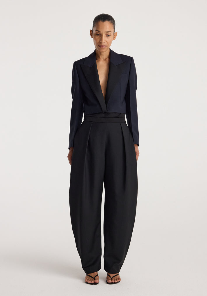 Woman wearing a tailored Cropped blazer | navy with a deep neckline paired with high-waisted wide-leg black trousers and strappy black sandals against a plain background