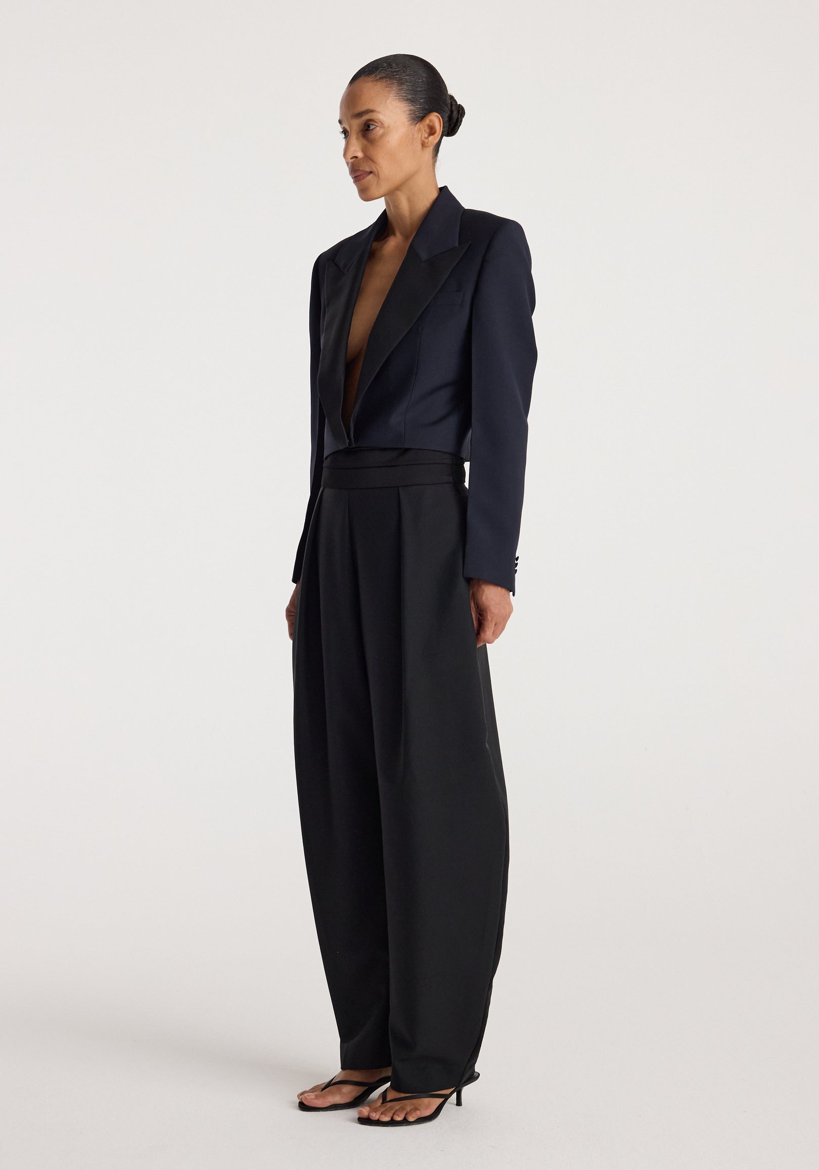 Woman wearing a tailored Cropped blazer | navy with wide-leg black trousers and black heeled sandals against a plain background.