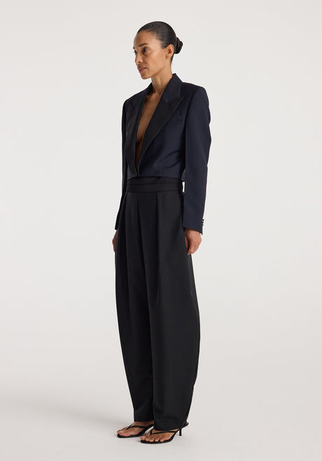Woman wearing a tailored Cropped blazer | navy with a deep neckline paired with high-waisted wide-leg black trousers and strappy black sandals against a plain background