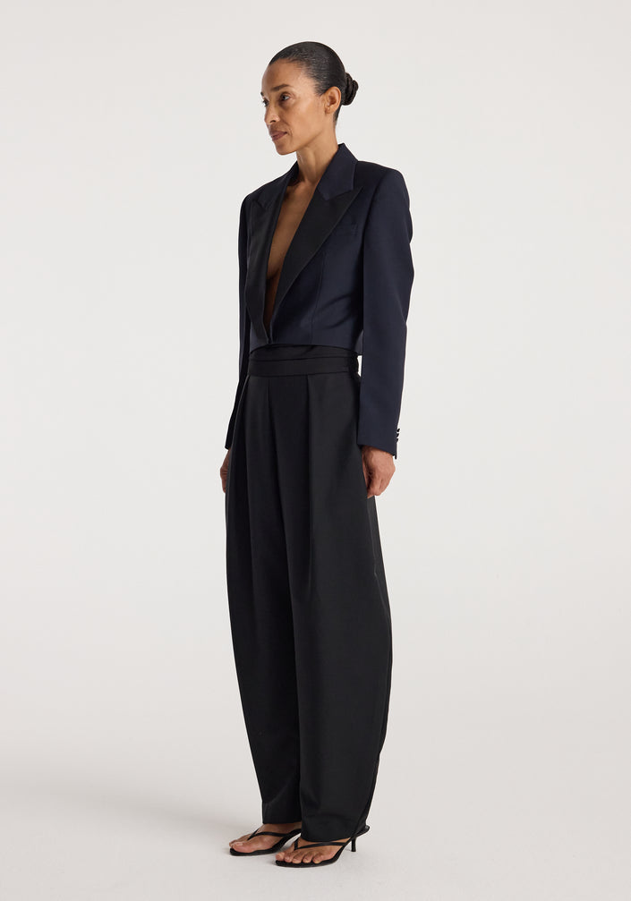 Woman wearing a tailored Cropped blazer | navy with a deep neckline paired with high-waisted wide-leg black trousers and strappy black sandals against a plain background
