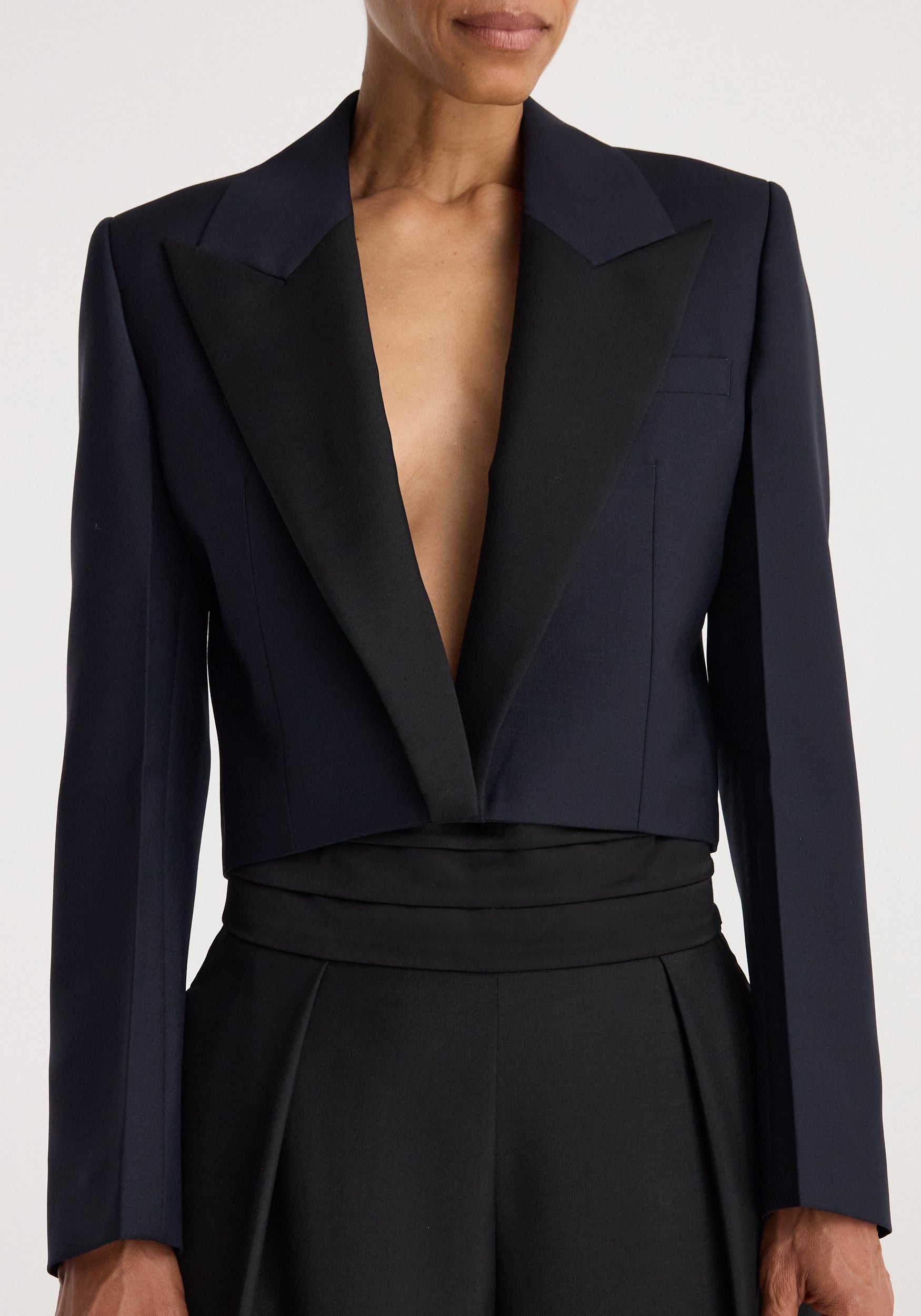 Woman wearing a tailored Cropped blazer | navy with a deep V-neck and structured shoulders, paired with high-waisted black pants against a neutral background.