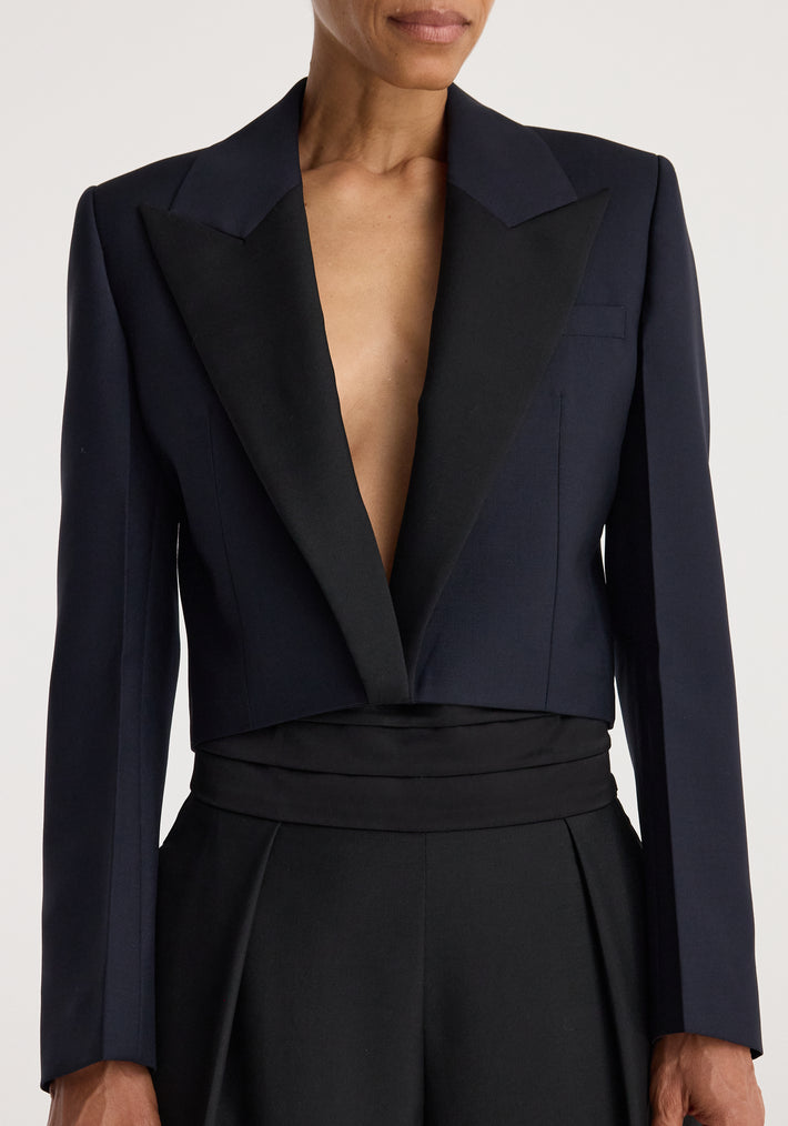 Woman wearing a tailored Cropped blazer | navy with a deep V-neck and structured shoulders, paired with high-waisted black pants against a neutral background.