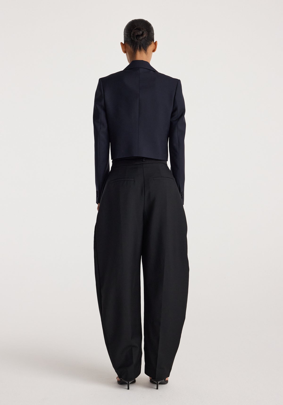 Woman seen from behind wearing a tailored Cropped blazer | navy paired with high-waisted, wide-leg black trousers and black heels against a plain background