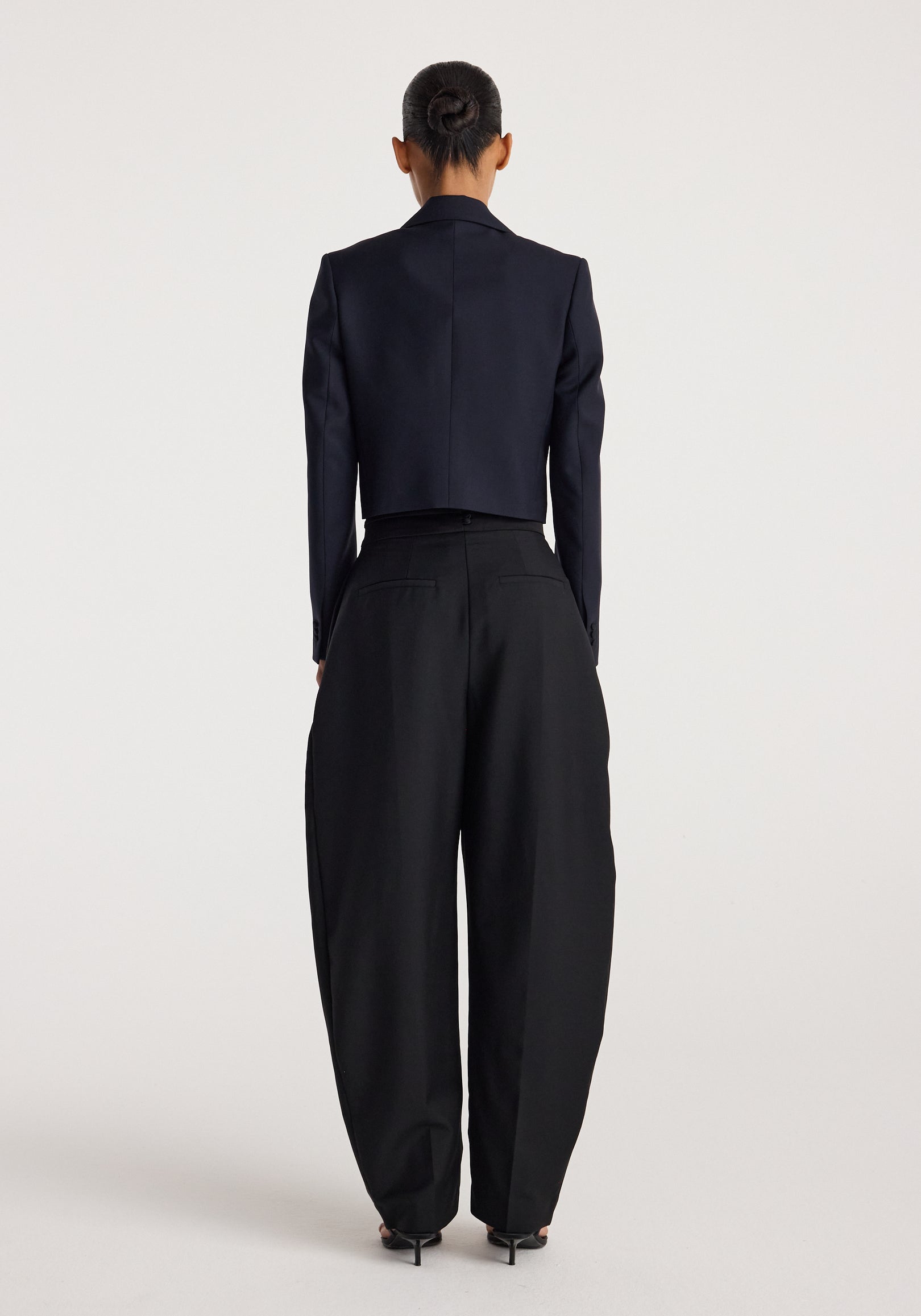 Woman seen from behind wearing a tailored Cropped blazer | navy paired with high-waisted, wide-leg black trousers and black heels against a plain background