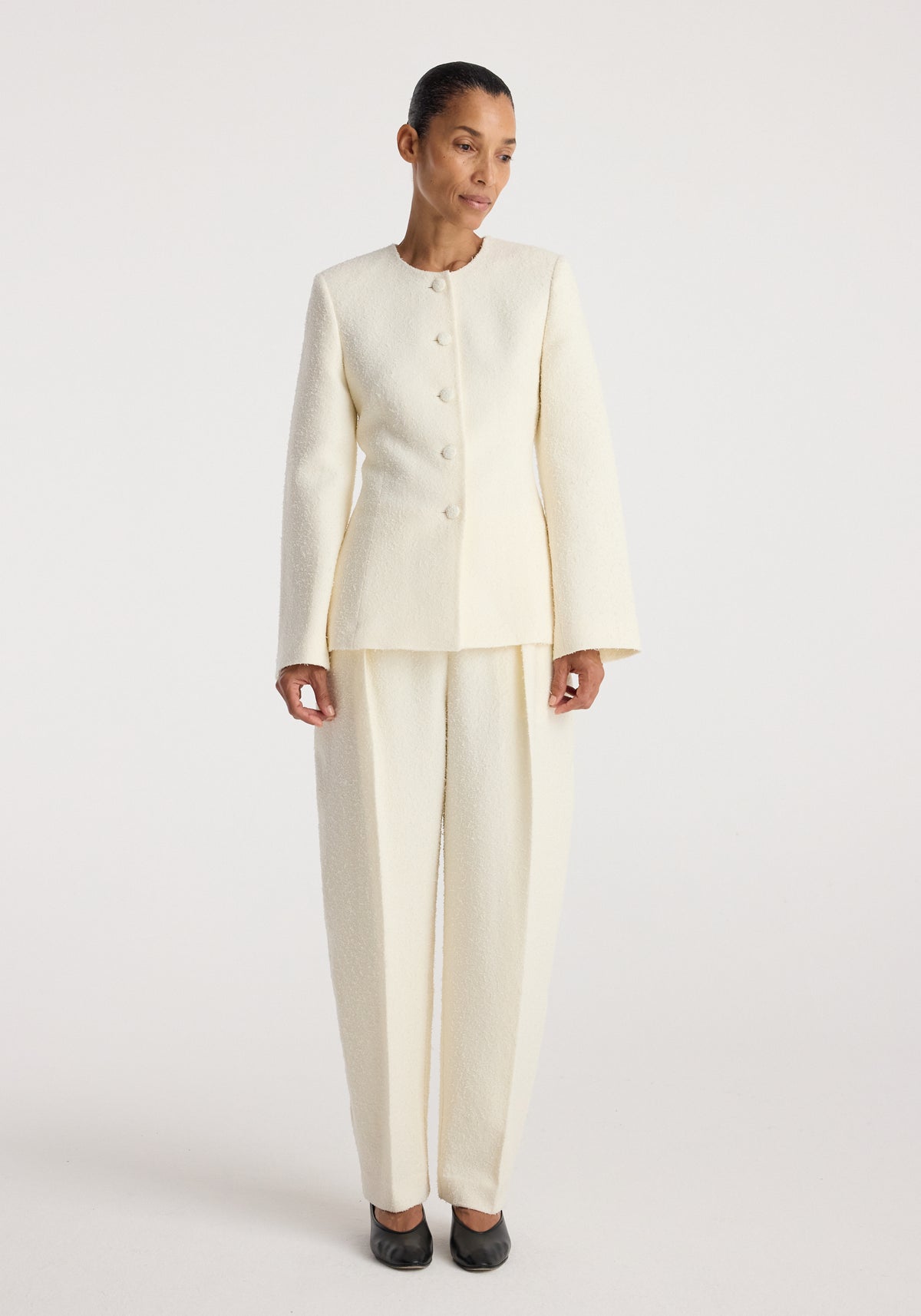 Woman wearing a cream textured bouclé shaped blazer | cream with matching wide-leg trousers, standing against a plain white background.