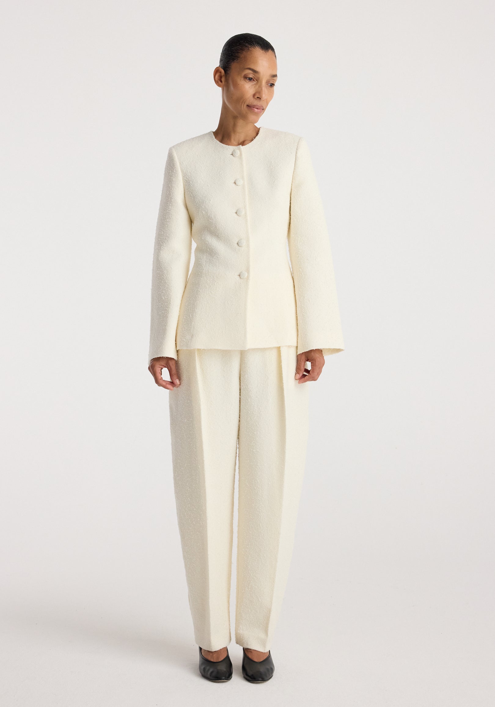 Woman wearing a cream textured bouclé shaped blazer | cream with matching wide-leg trousers, standing against a plain white background.