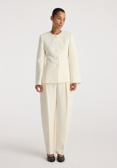 Woman wearing a cream textured bouclé shaped blazer | cream with matching wide-leg trousers, standing against a plain white background.