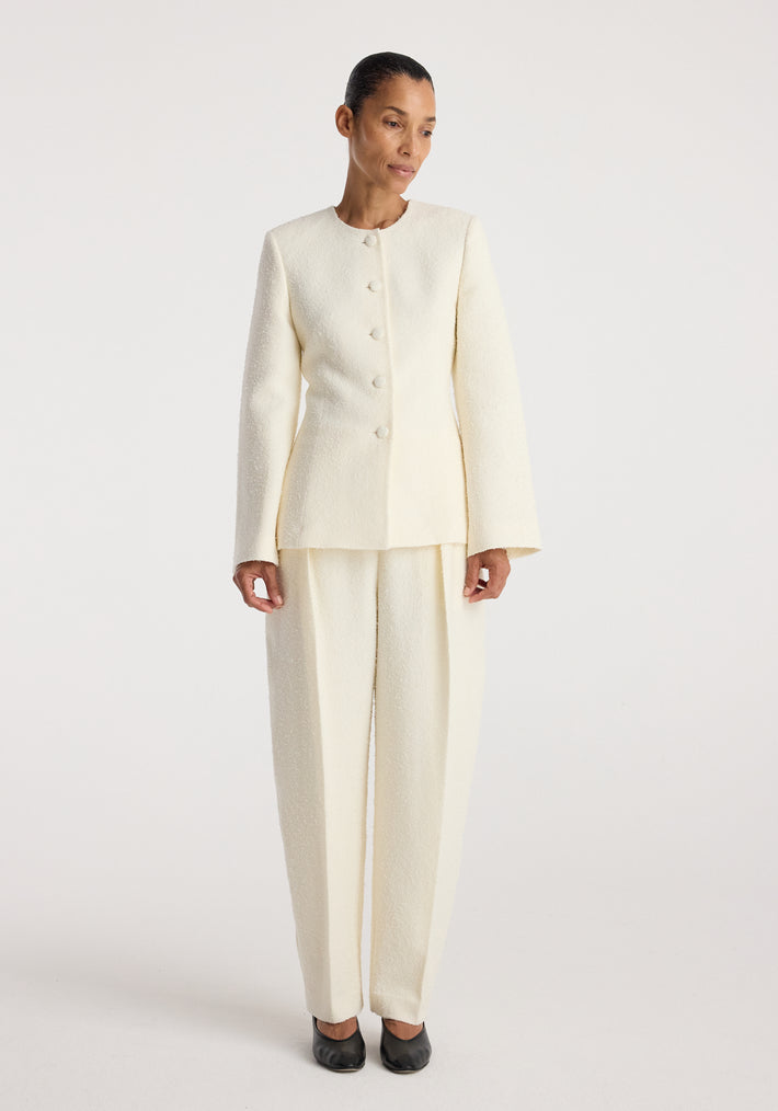 Woman wearing a cream textured bouclé shaped blazer | cream with matching wide-leg trousers, standing against a plain white background.