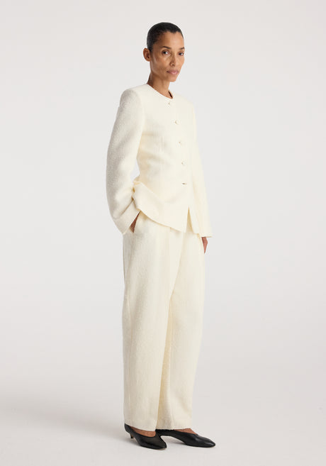 Woman wearing a cream textured bouclé shaped blazer | cream with matching wide-leg trousers, standing against a plain white background.