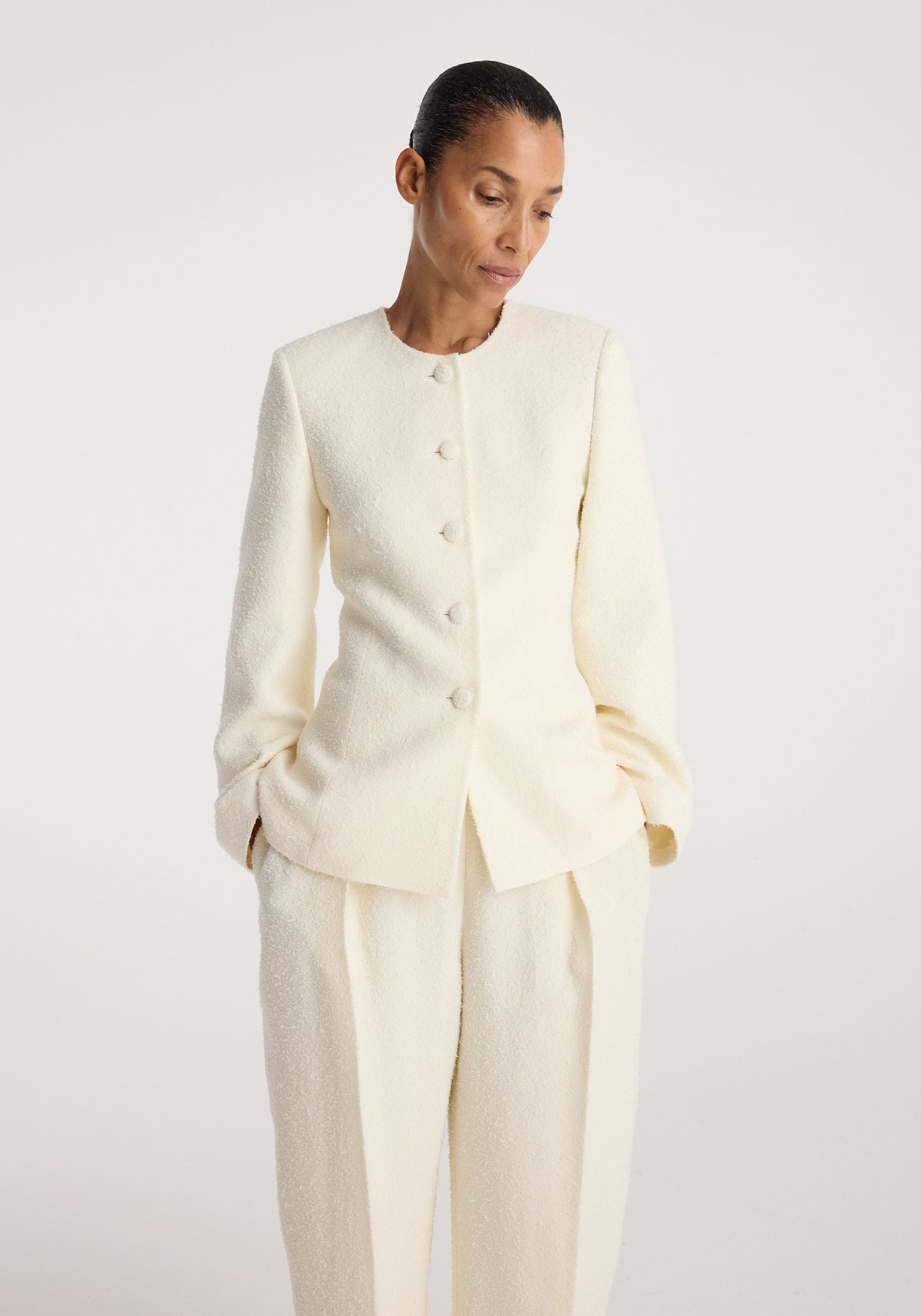 Woman wearing a cream textured long-sleeve buttoned Bouclé shaped blazer | cream with matching loose pants, posing against a plain light background.