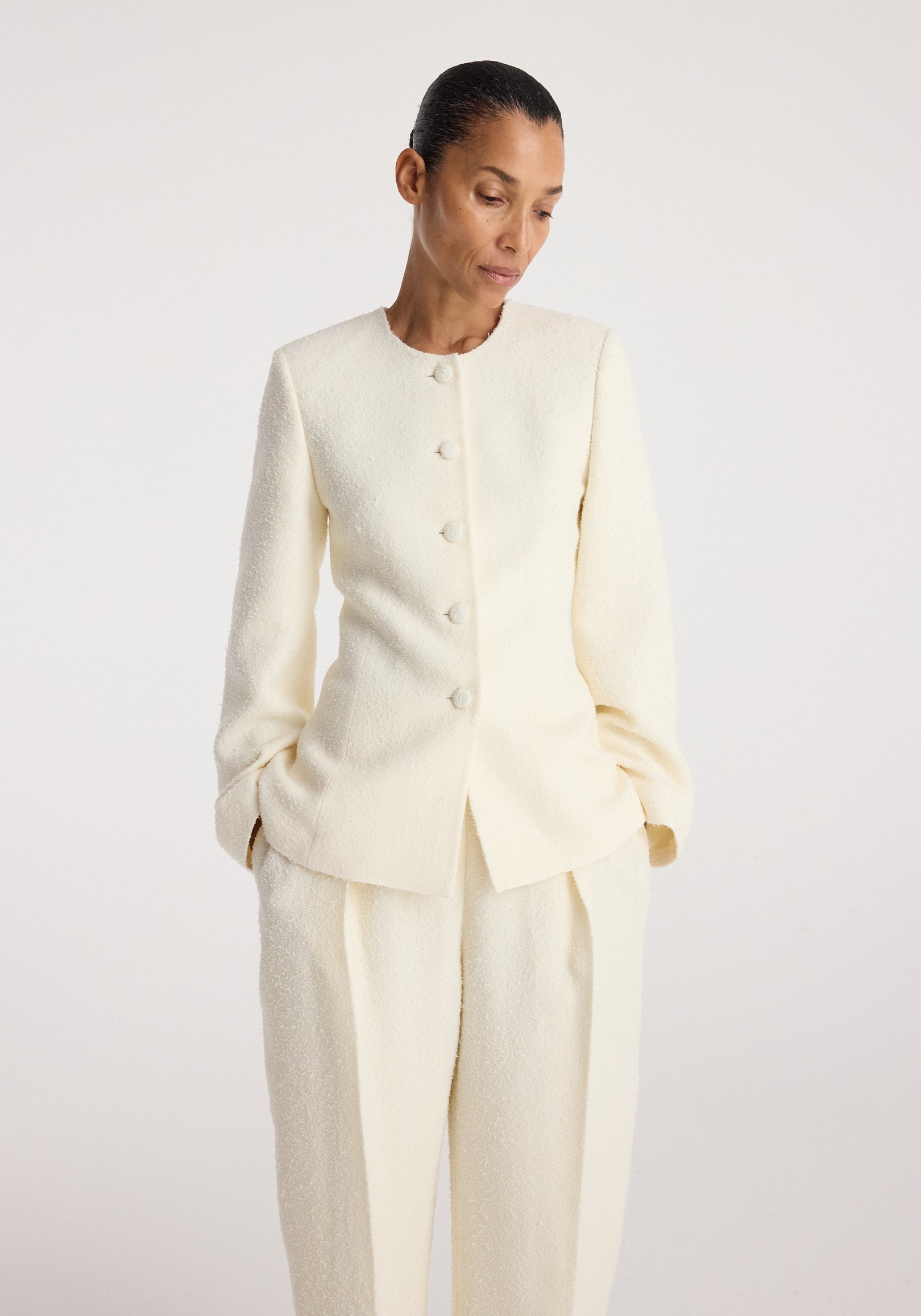 Woman wearing a cream textured long-sleeve buttoned Bouclé shaped blazer | cream with matching loose pants, posing against a plain light background.