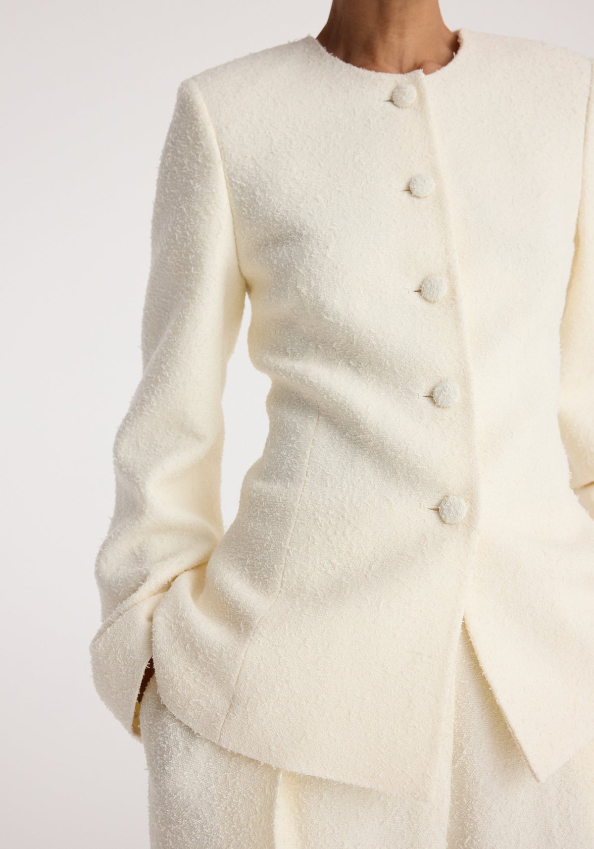 Close-up of a person wearing a cream textured bouclé shaped blazer | cream with fabric-covered buttons and a tailored fit.
