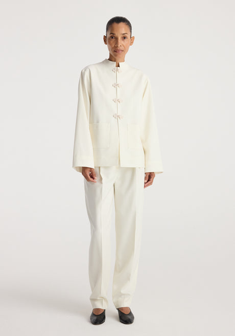Woman wearing a minimalist off-white Pankou closure jacket | off white with long sleeves and front knot closures, paired with matching trousers and black flats.