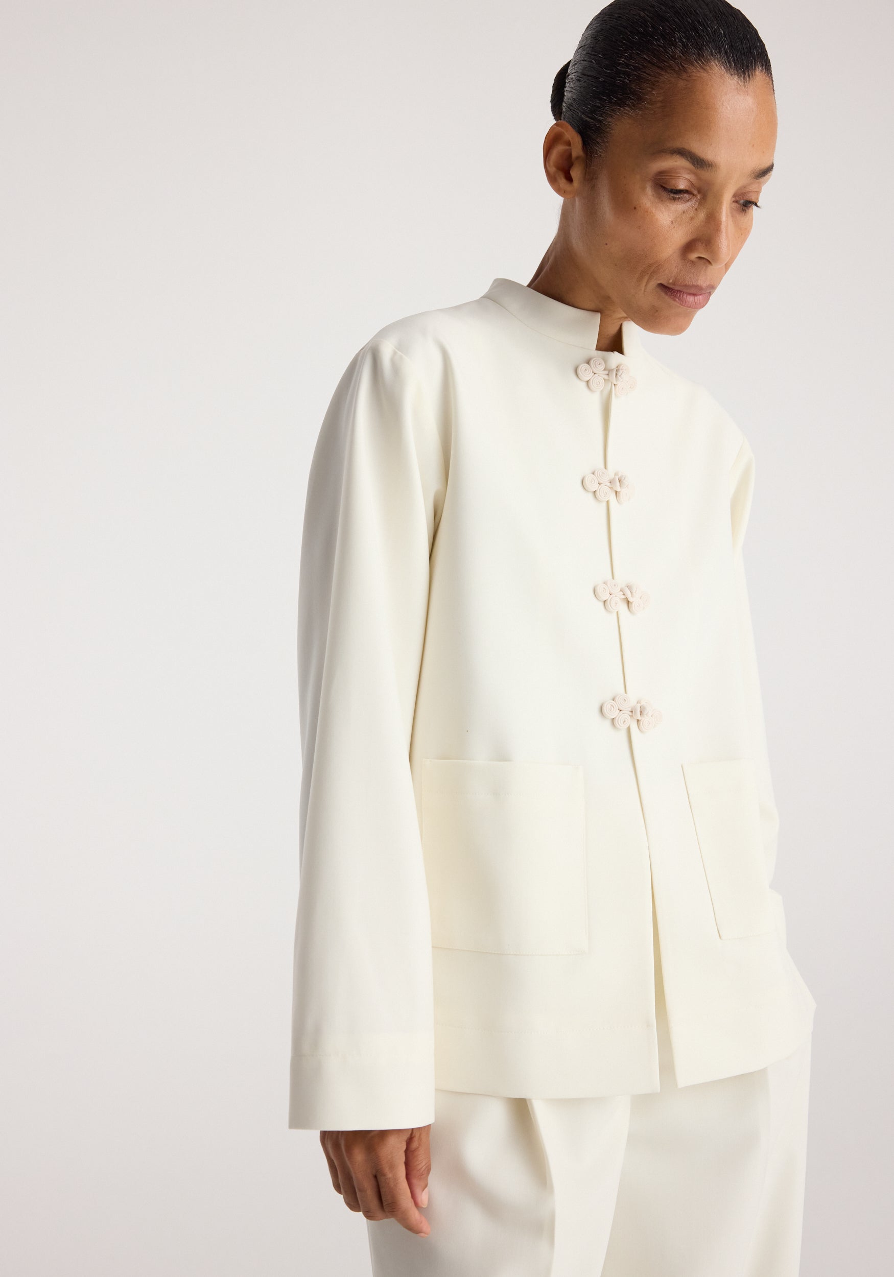 Woman wearing an off white Pankou closure jacket | off white with decorative knot fastenings and front patch pockets against a neutral background