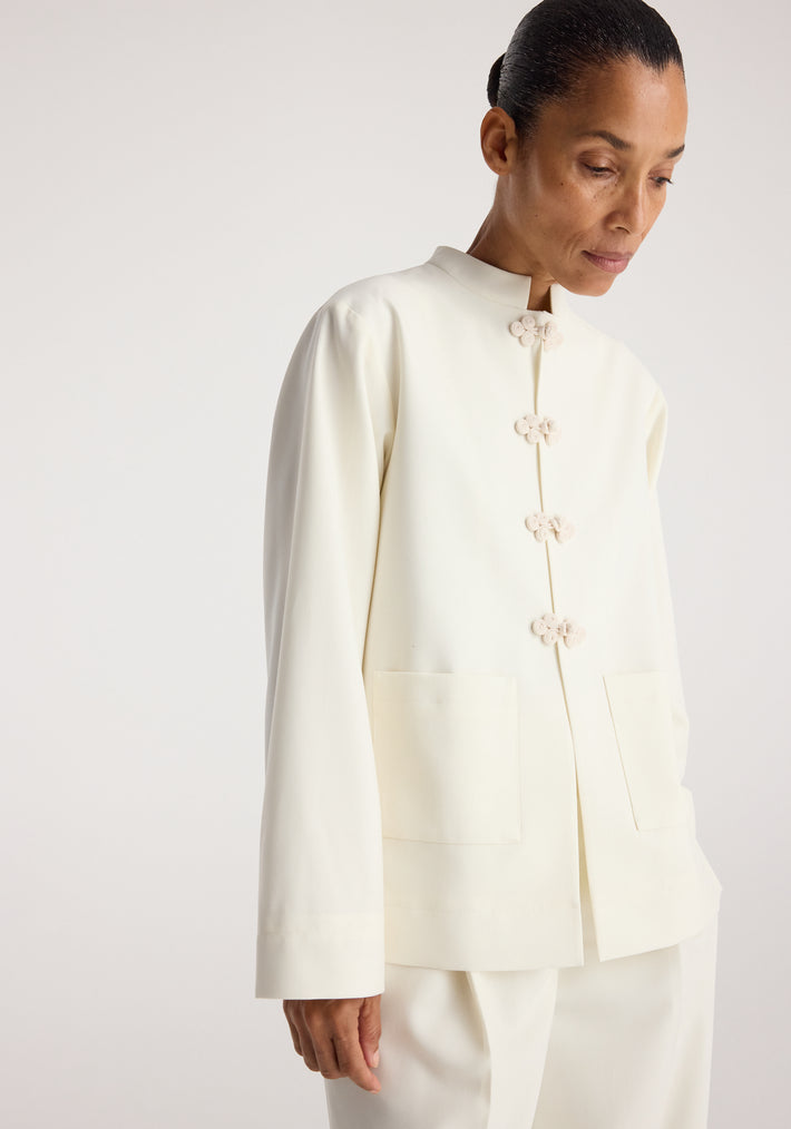 Woman wearing an off white Pankou closure jacket | off white with decorative knot fastenings and front patch pockets against a neutral background
