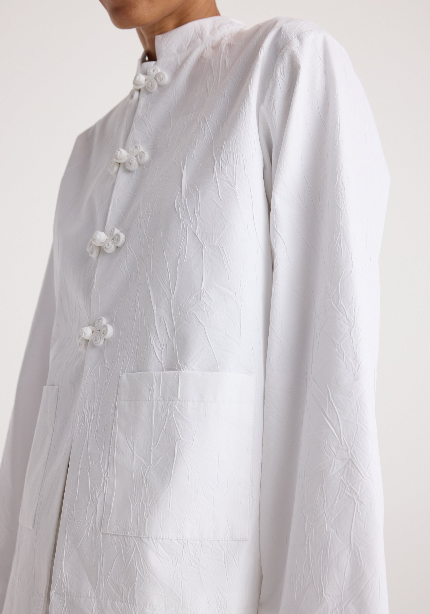 Close-up of a white textured jacket featuring a pankou closure with knotted buttons and front patch pockets, showcasing the Pankou closure crushed jacket | optic white design.