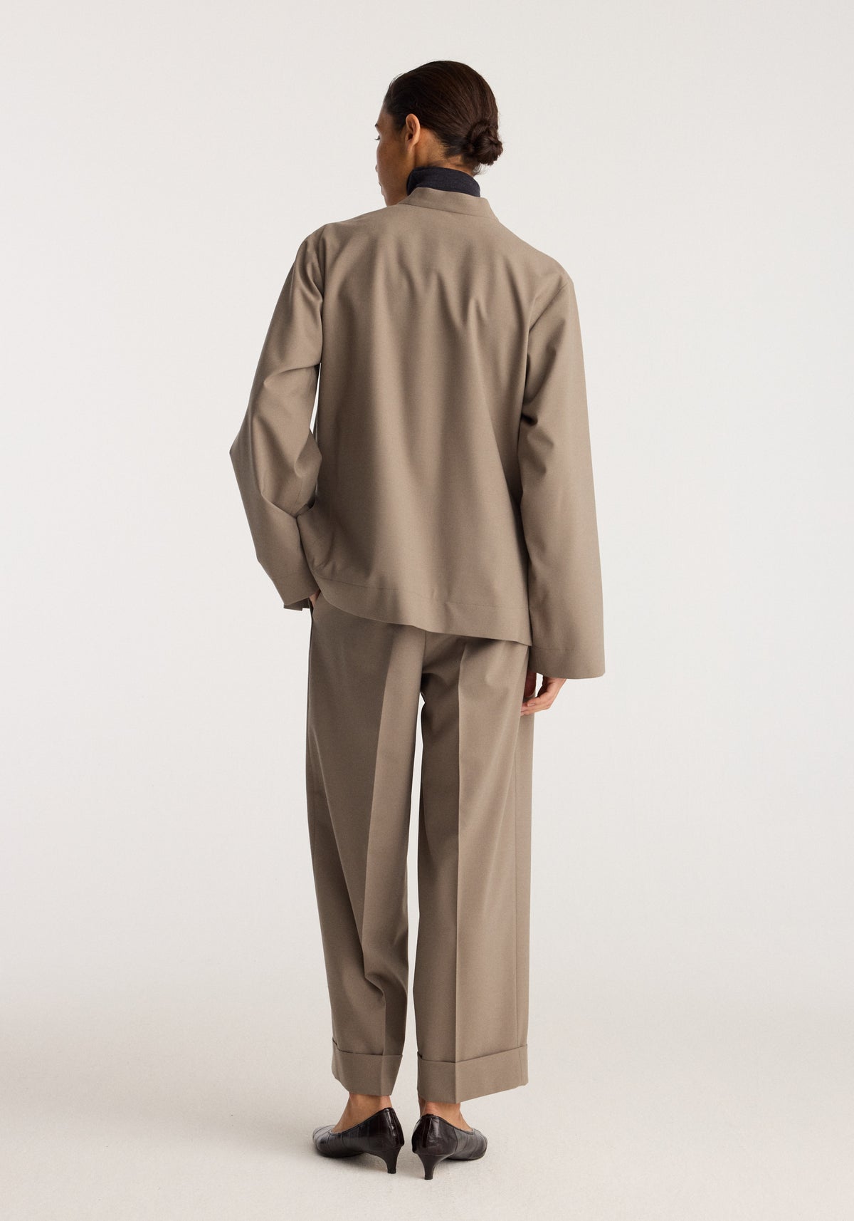 Pankou closure jacket | taupe seen from the back on a model, featuring a stand collar, long sleeves, relaxed fit, matching trousers, and black shoes