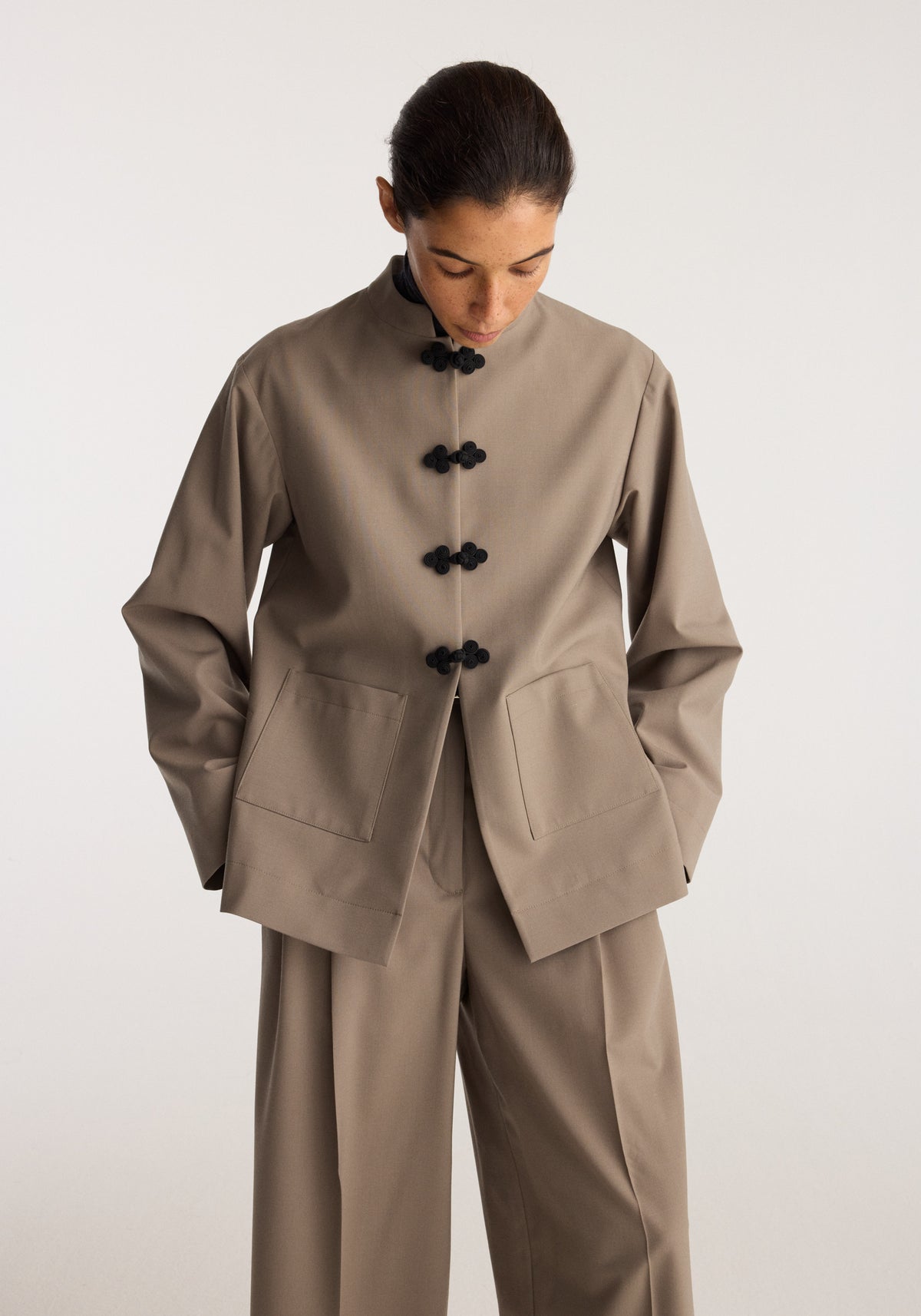 Pankou closure jacket | taupe shown on a model with black knot closures front pockets and relaxed sleeves in a minimalist studio setting