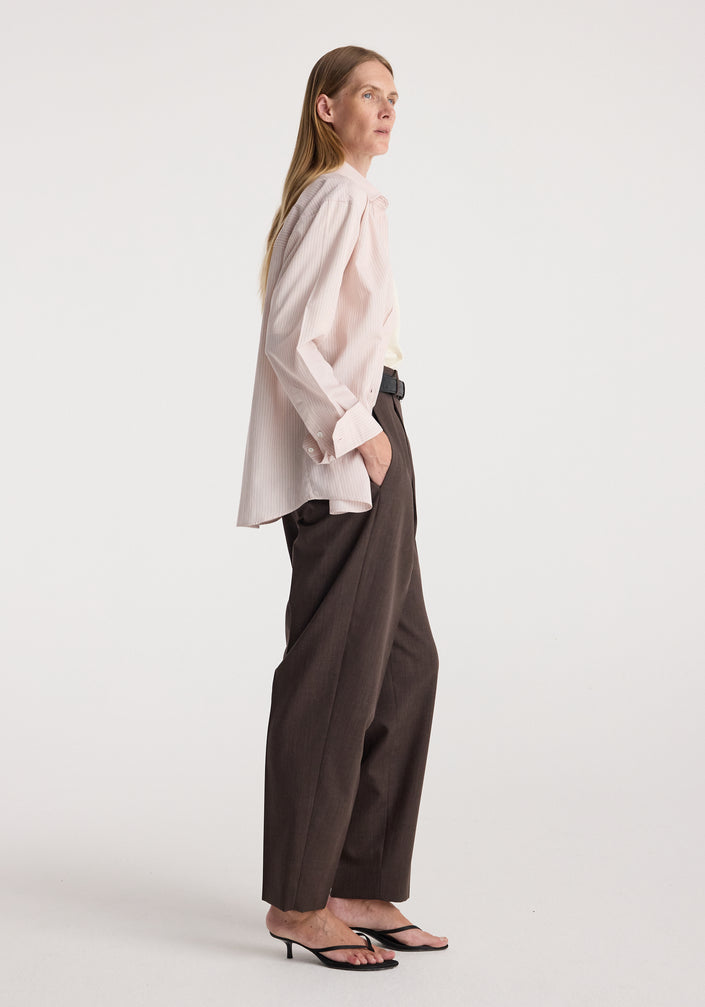 Woman wearing a Classic fit striped shirt | rose stripe in light pink over a white top, paired with high-waisted dark brown pants and black heeled sandals against a plain background.