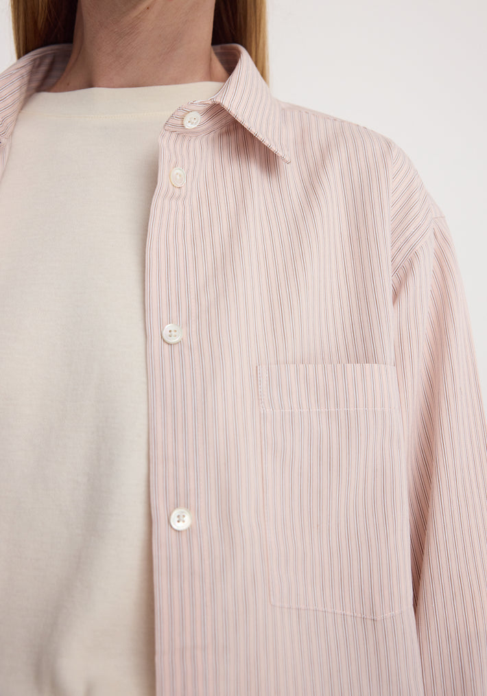 Close-up of a person wearing a Classic fit striped shirt | rose stripe with thin vertical stripes, buttoned down the front and featuring a chest pocket, layered over a white top.