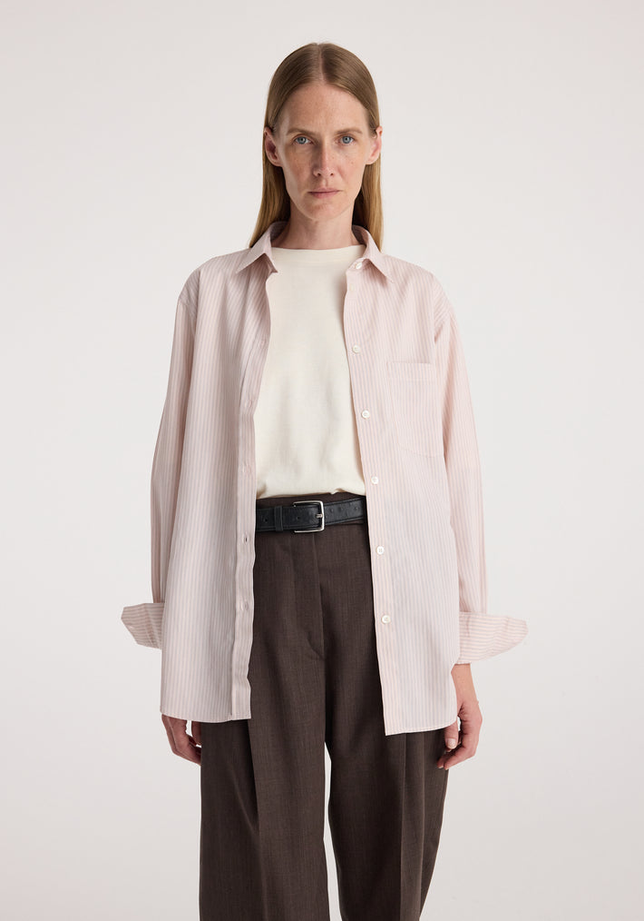 Woman wearing a Classic fit striped shirt | rose stripe, unbuttoned over a white top with brown high-waisted pants and a black belt in a neutral studio setting.