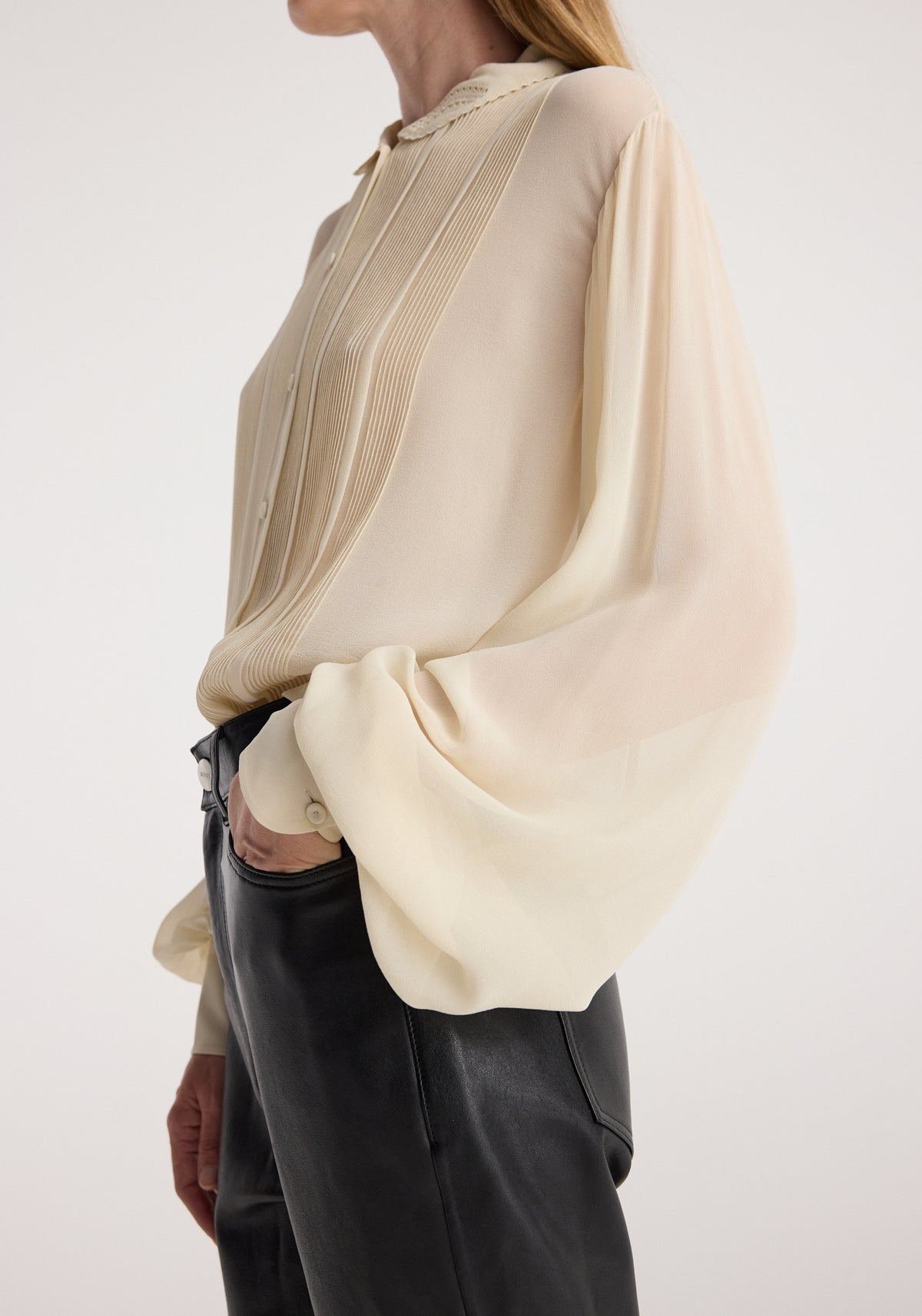 Woman wearing a Romantic top | cream featuring long, billowy sleeves, pleated front detail, and a delicate collar, paired with high-waisted black leather pants.