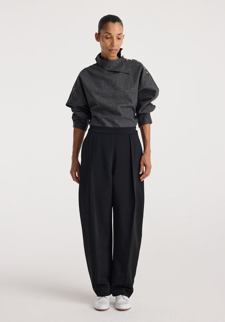 Woman wearing a grey slub textured top with a high, asymmetrical collar and button details on the shoulder, paired with loose black trousers and white shoes, styled in the Reimagined collar top | grey slub.