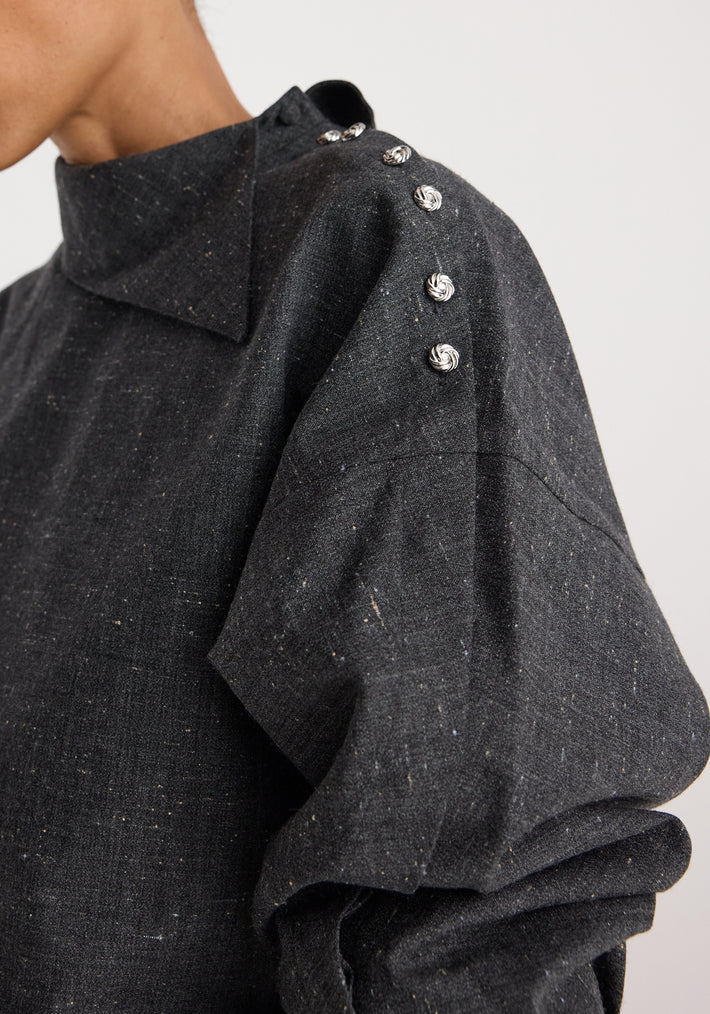 Close-up of a person wearing a Reimagined collar top | grey slub featuring a high collar and silver decorative buttons along the shoulder seam on textured grey fabric.