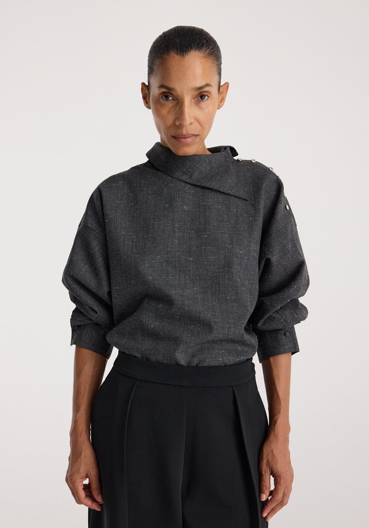 Woman wearing Reimagined collar top | grey slub with a unique asymmetrical collar and button details on the shoulder, paired with black high-waisted pants.
