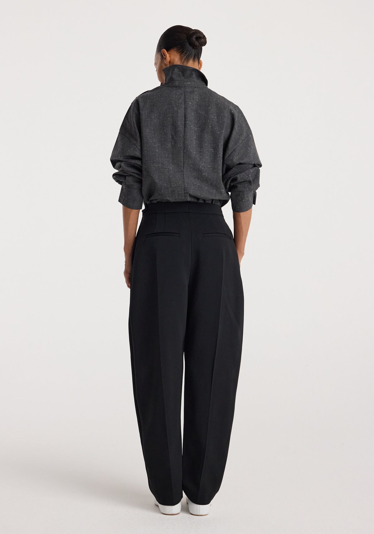 Woman seen from behind wearing a dark gray textured top with a high collar and long sleeves, paired with loose black pants and white shoes, modeling Reimagined collar top | grey slub.