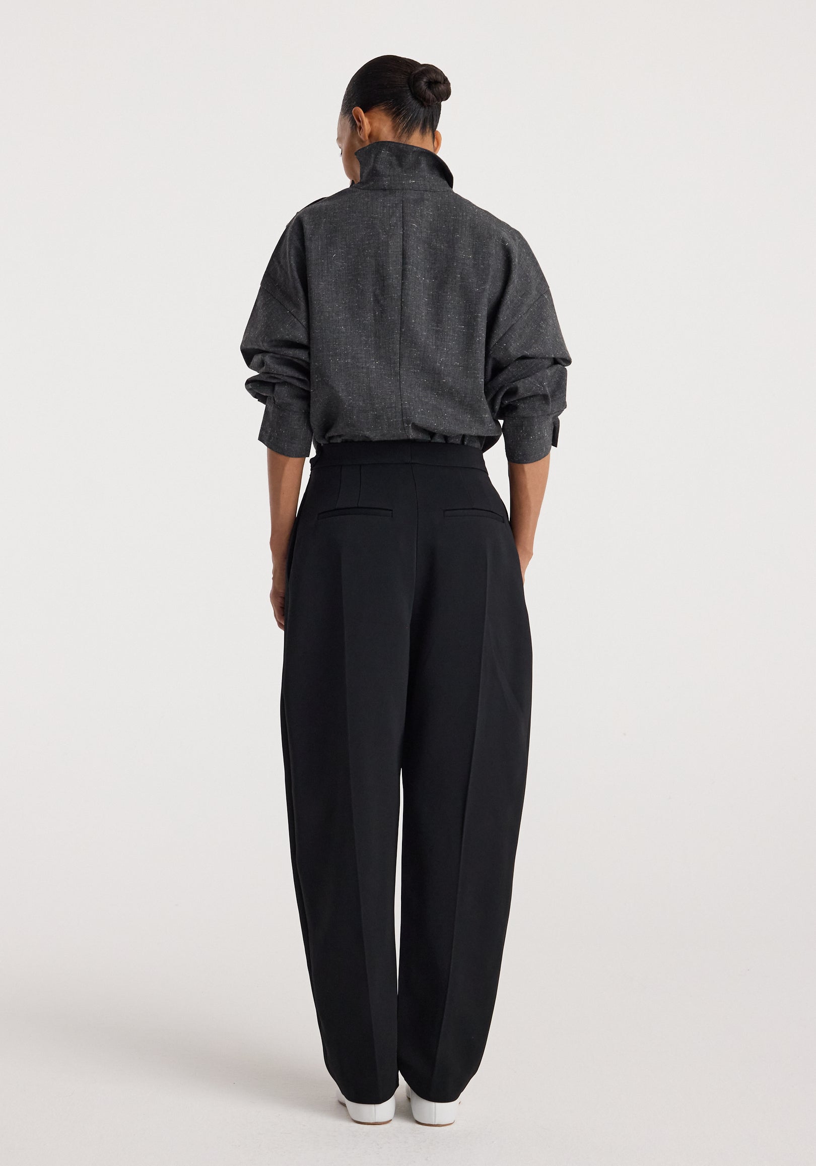 Woman seen from behind wearing a dark gray textured top with a high collar and long sleeves, paired with loose black pants and white shoes, modeling Reimagined collar top | grey slub.