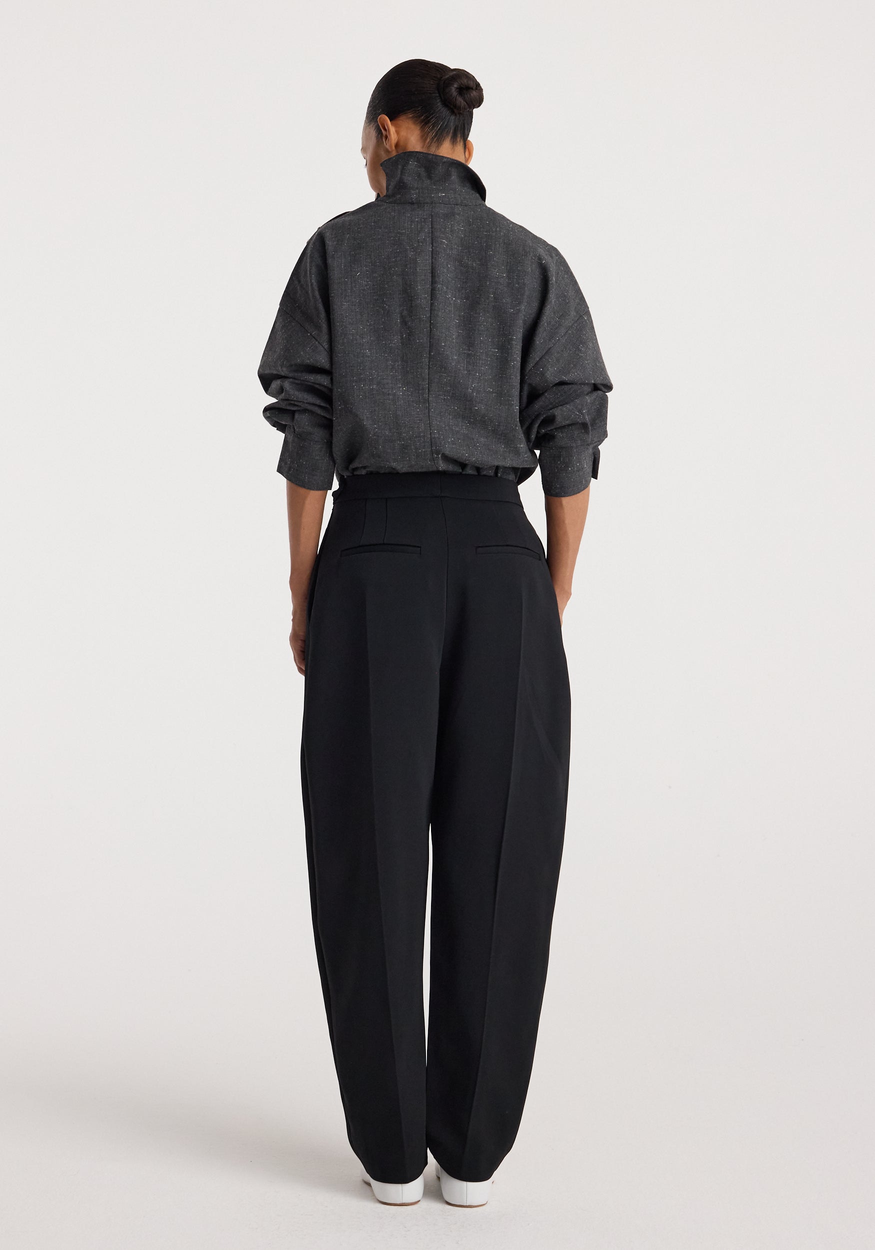Woman seen from behind wearing a dark gray textured top with a high collar and long sleeves, paired with loose black pants and white shoes, modeling Reimagined collar top | grey slub.