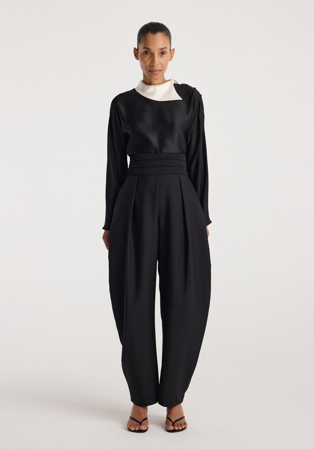 Woman wearing a black top with a contrasting white reimagined collar and long sleeves paired with high-waisted, pleated black pants and black sandals, featuring the Reimagined collar top | black.