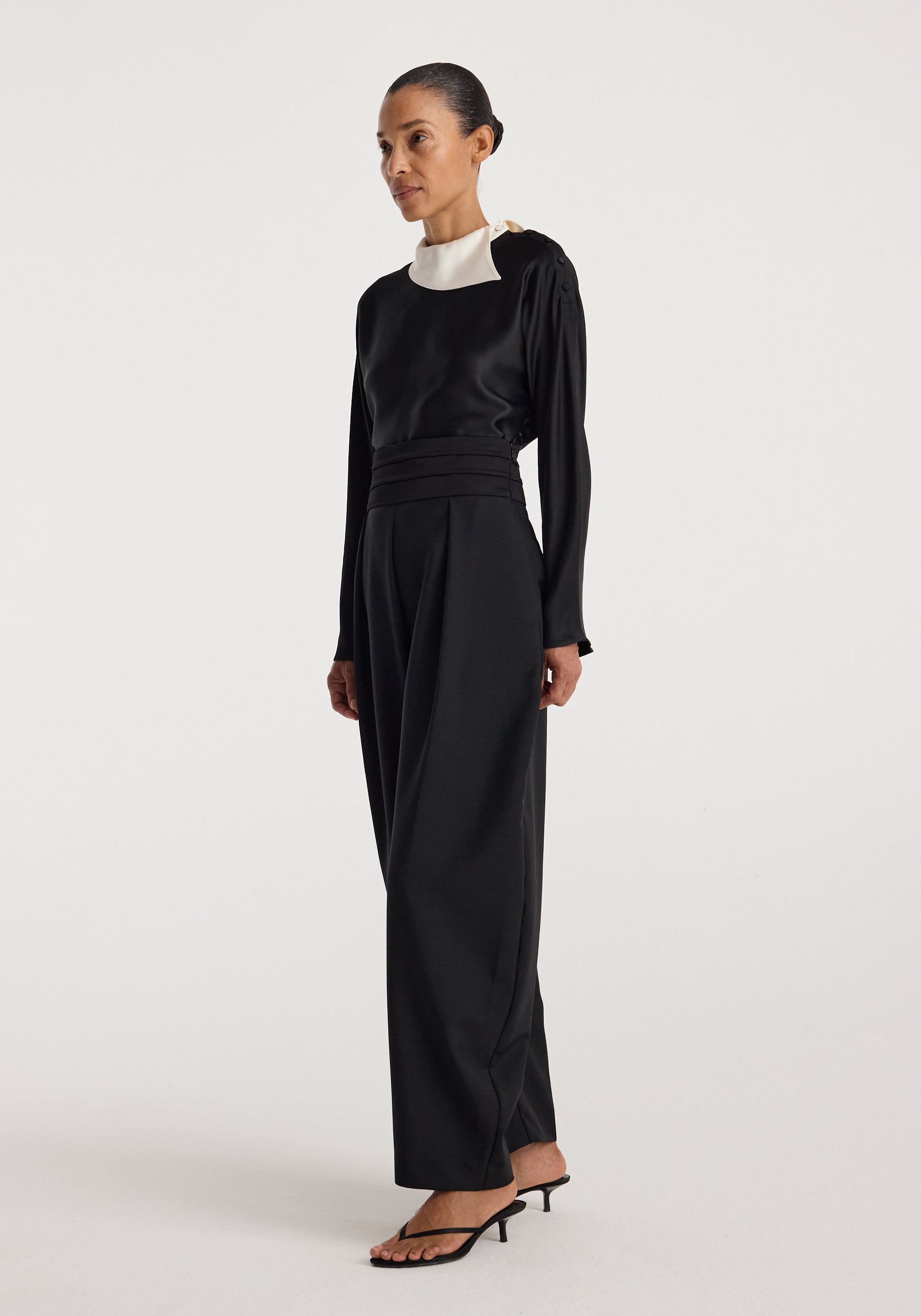 Woman wearing a black long-sleeve top with a unique white collar detail and wide-leg black pants, styled with black heeled sandals, showcasing the Reimagined collar top | black.