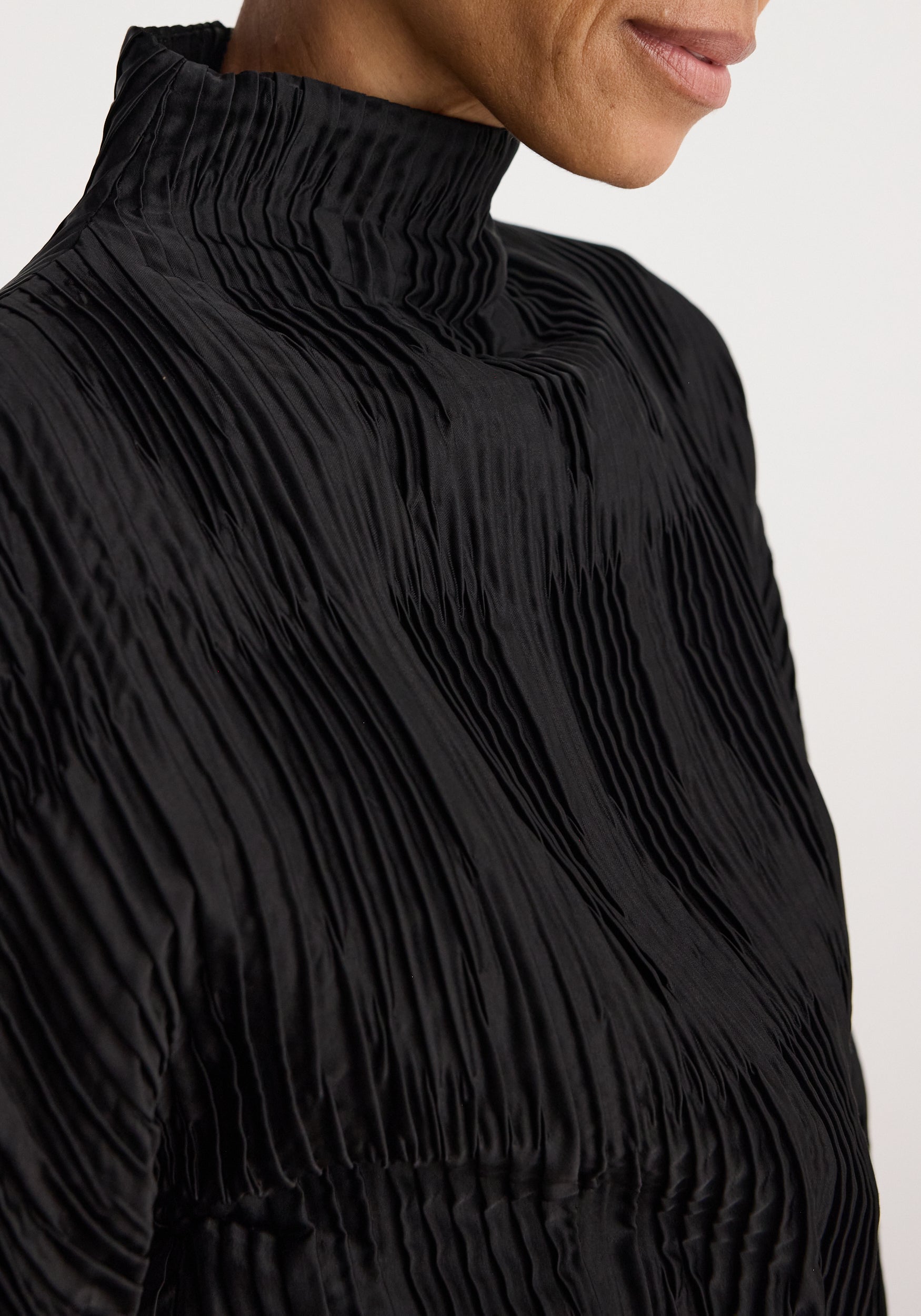 Close-up of a person wearing a black Plissé shaped top | black featuring finely pleated fabric and a high neckline.