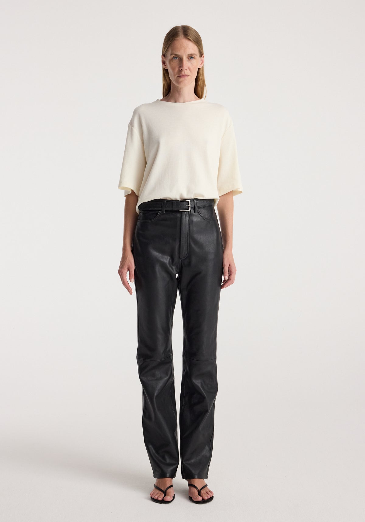 Woman wearing an Oversized cotton wool t-shirt | cream paired with high-waisted black pants and black sandals, standing against a plain light background.