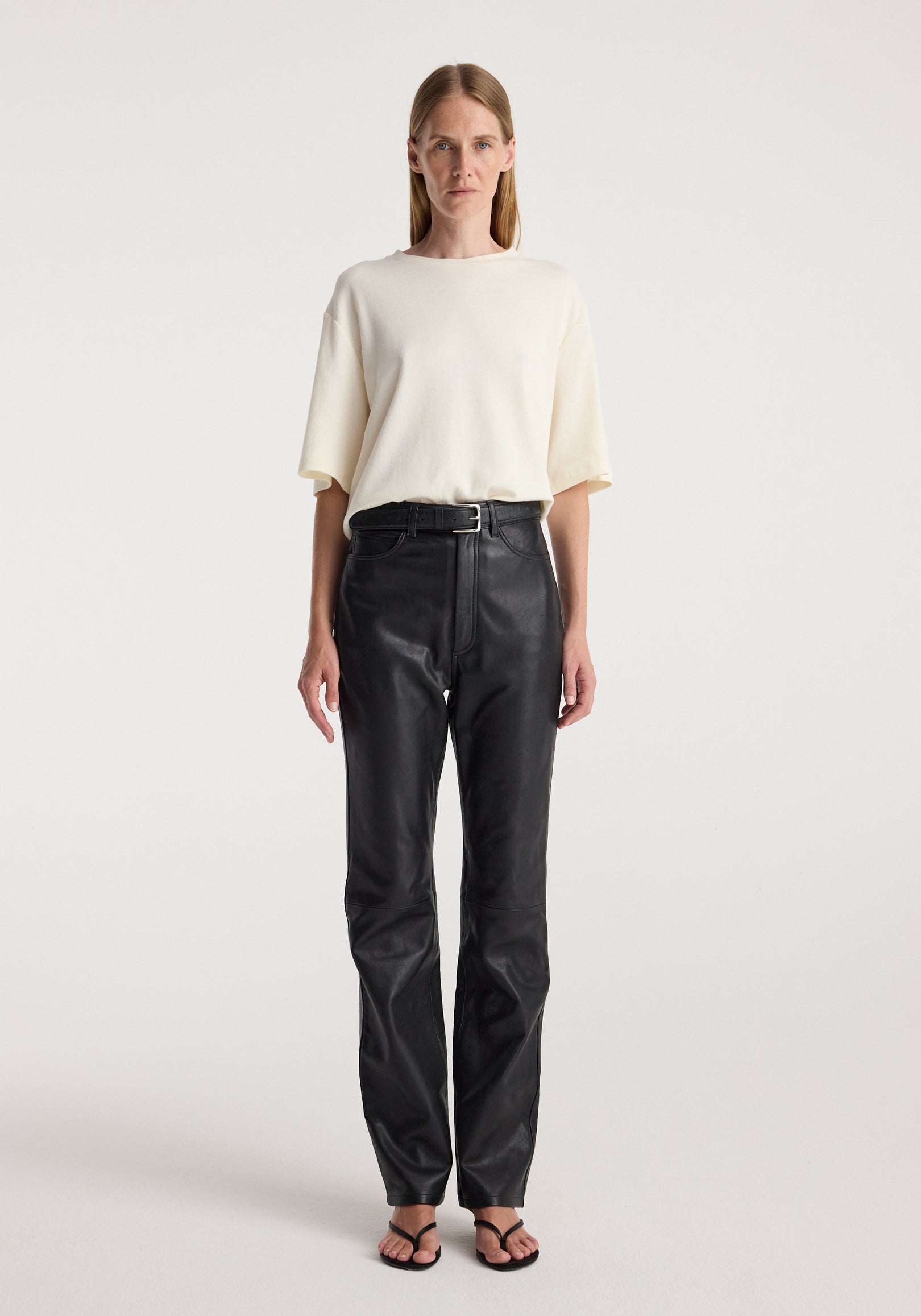 Woman wearing an Oversized cotton wool t-shirt | cream paired with high-waisted black pants and black sandals, standing against a plain light background.