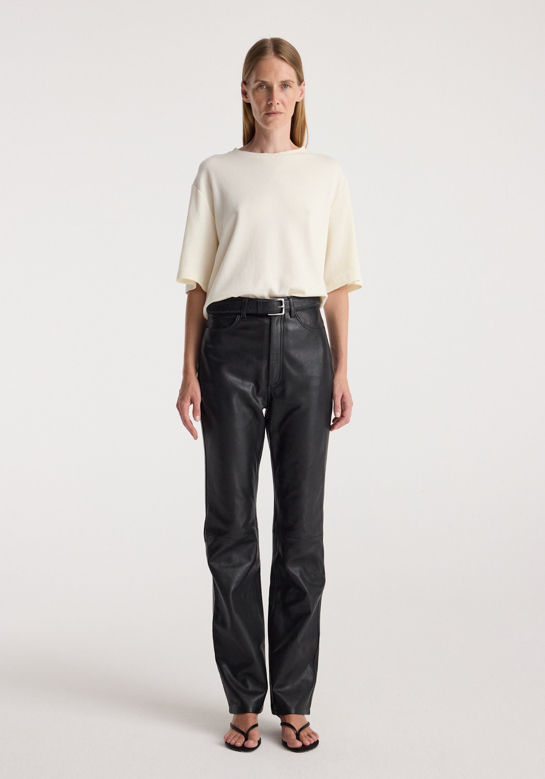 Woman wearing an Oversized cotton wool t-shirt | cream paired with high-waisted black pants and black sandals, standing against a plain light background.