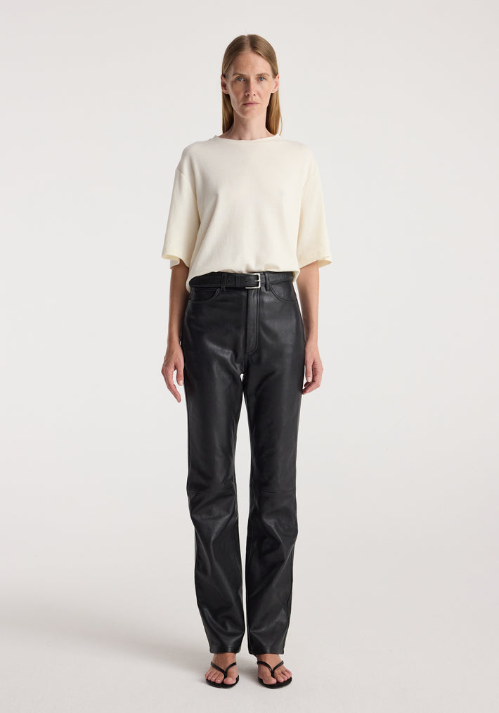 Woman wearing an Oversized cotton wool t-shirt | cream paired with high-waisted black pants and black sandals, standing against a plain light background.