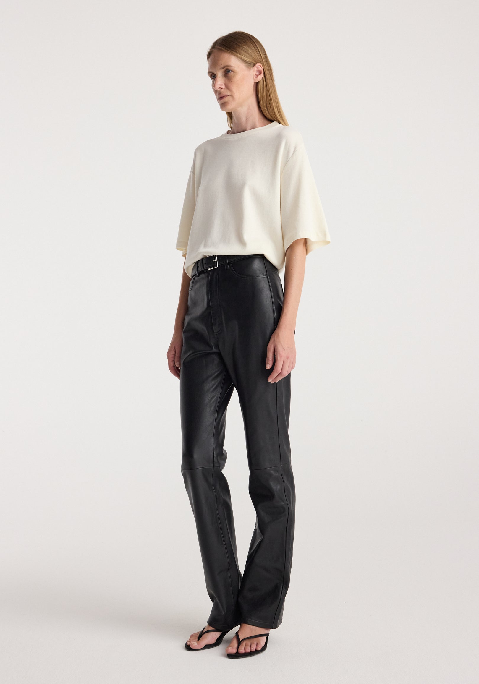 Woman wearing an oversized cotton wool t-shirt | cream paired with black leather pants and black open-toe heels, standing against a plain light background.