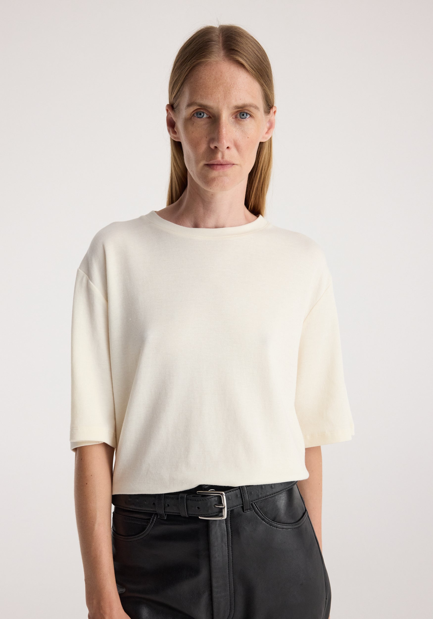 Woman wearing an oversized cotton wool t-shirt | cream with a round neckline and short sleeves paired with black pants and a belt against a plain background