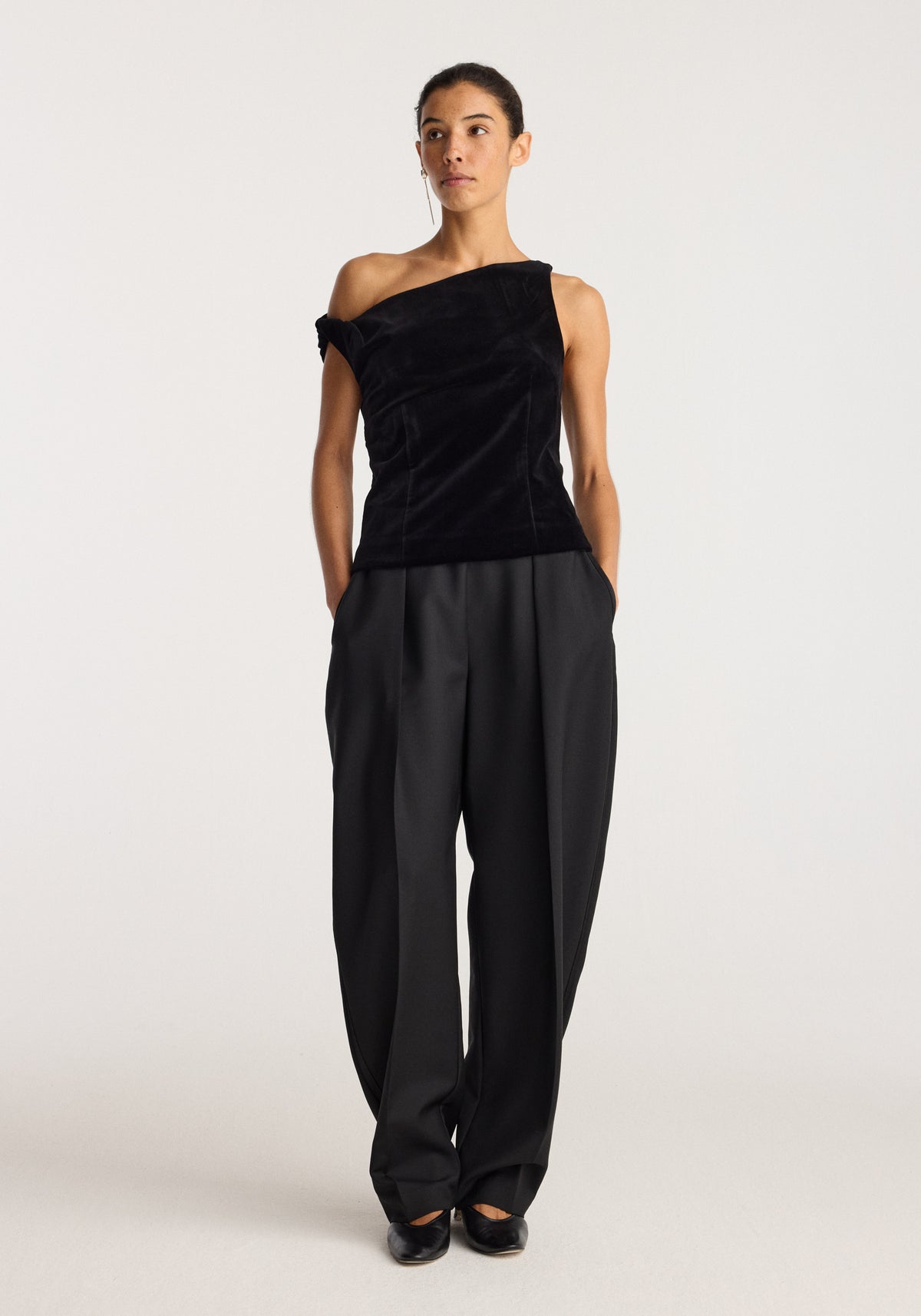 Draped velvet top | black worn by a model with an asymmetric neckline and draped silhouette, styled with wide leg black trousers.